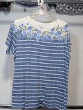 A short-sleeve crewneck t-shirt hanging on a clear plastic hanger. The shirt features a blue and white horizontal stripe pattern across the body, with a white yoke at the shoulders decorated with a blue and green floral print.