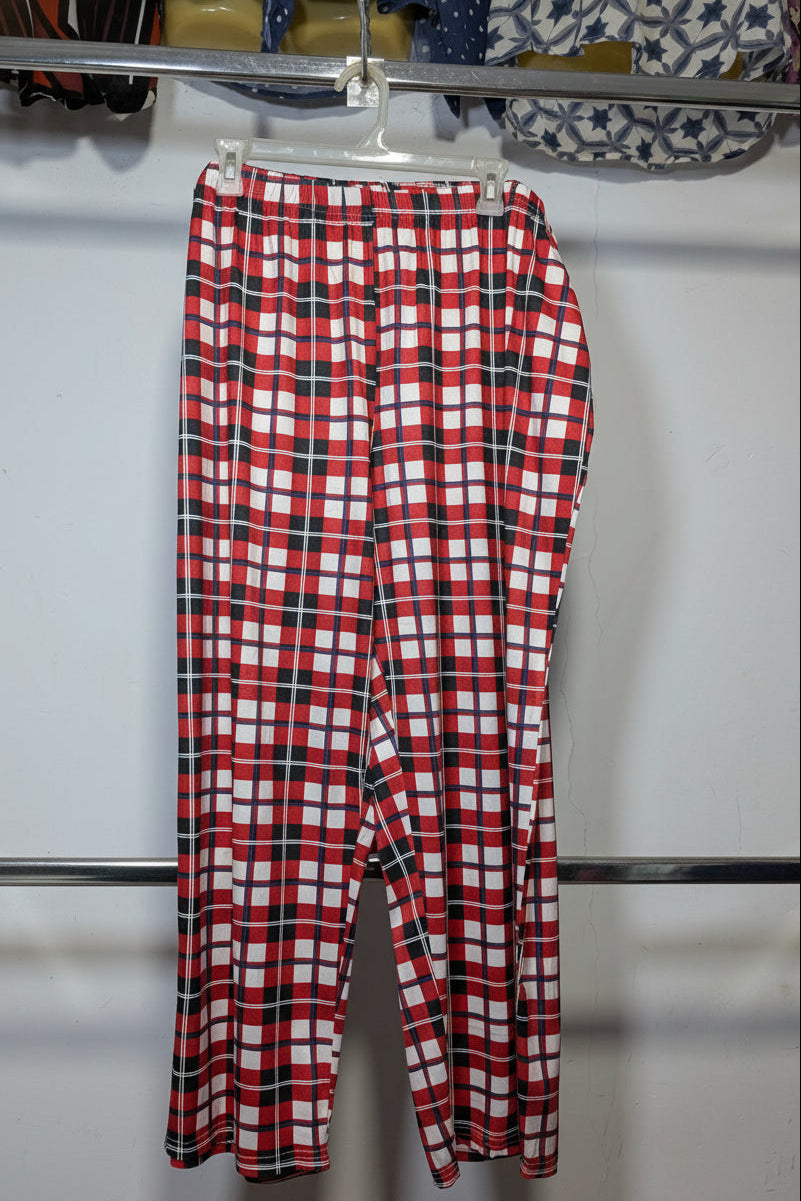 Red, white, and black plaid cropped pants hanging on a white plastic hanger from a metal clothing rack.