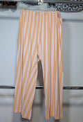 Orange and white vertically striped cropped pants hanging on a white plastic hanger from a clothing rack.