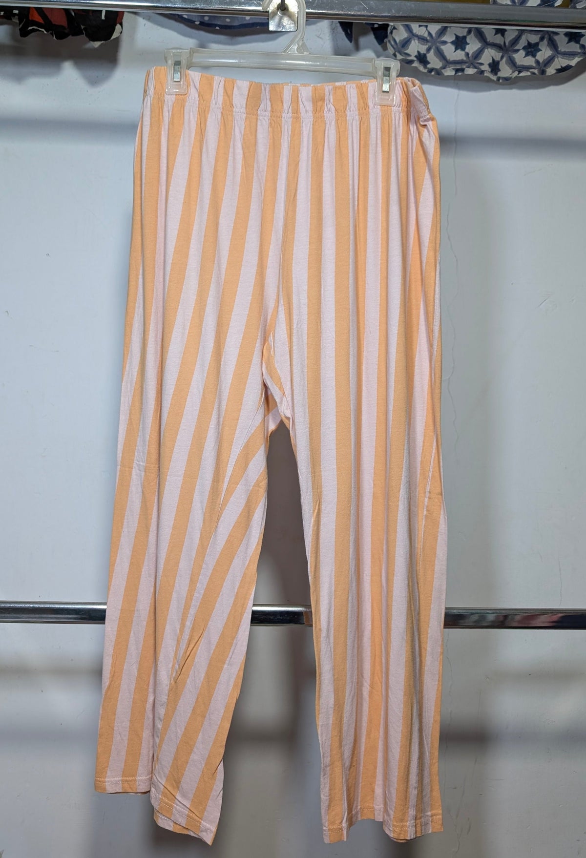 Orange and white vertically striped cropped pants hanging on a white plastic hanger from a clothing rack.