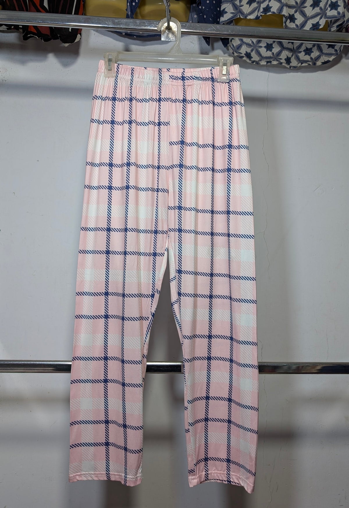 Pink and white plaid pants hanging on a metal rack against a white wall.