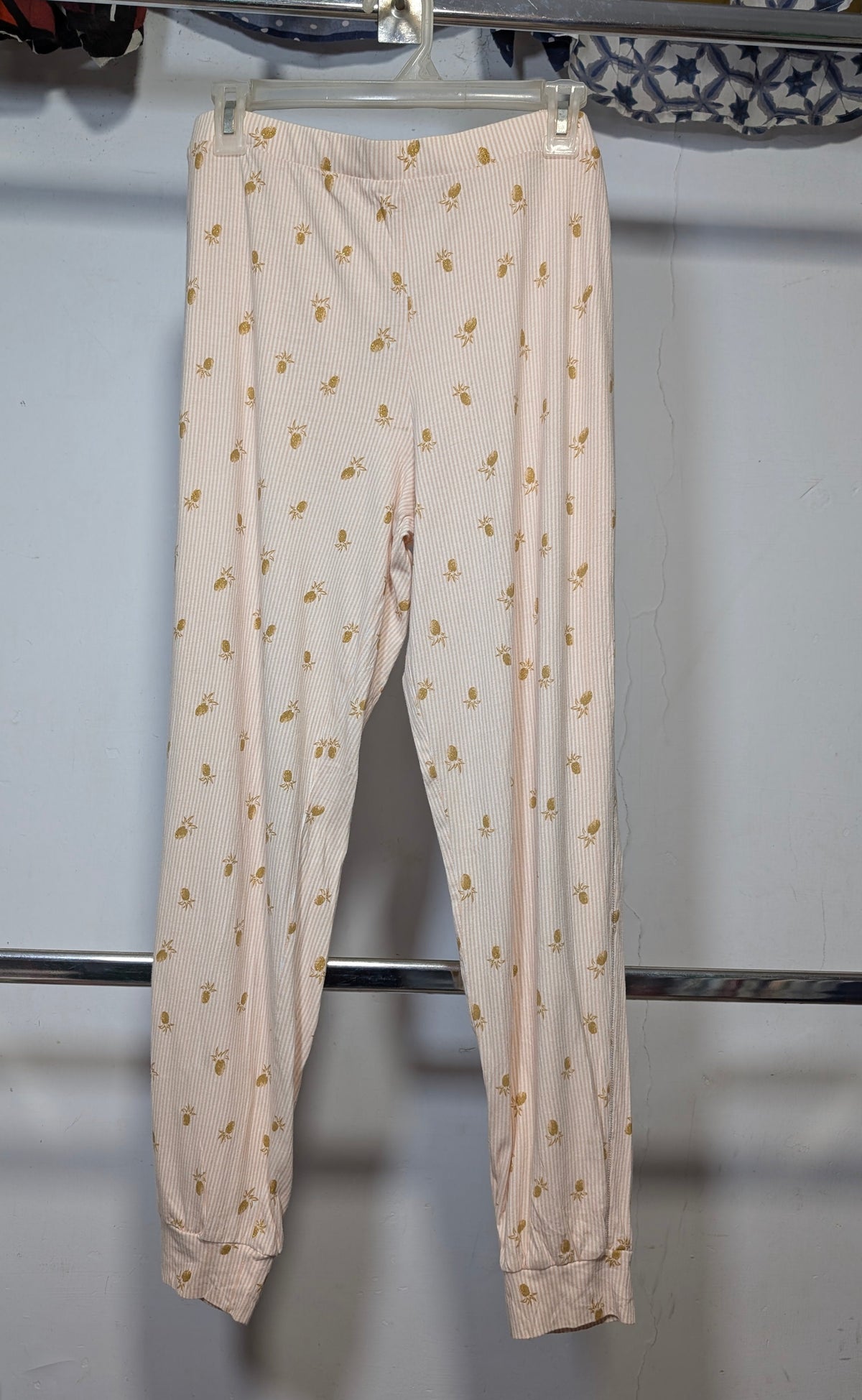 A pair of light pink jogger pants with a small yellow floral pattern, hanging on a plastic hanger from a clothing rack.