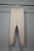 A pair of light pink jogger-style pants with a small yellow floral pattern, hanging from a clear plastic hanger on a metal clothing rack against a plain gray wall.