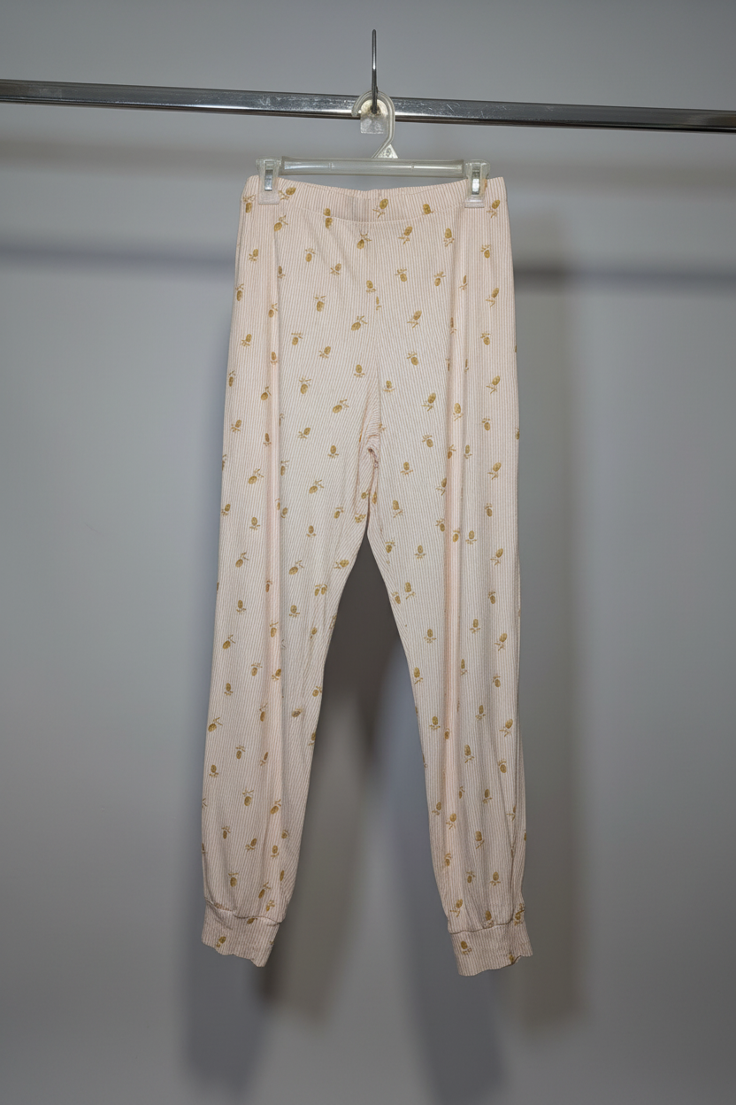 A pair of light pink jogger-style pants with a small yellow floral pattern, hanging from a clear plastic hanger on a metal clothing rack against a plain gray wall.
