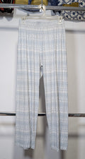 Light blue and white patterned wide-leg pants hanging on a hanger from a clothing rack, set against a white wall with other garments visible in the background.