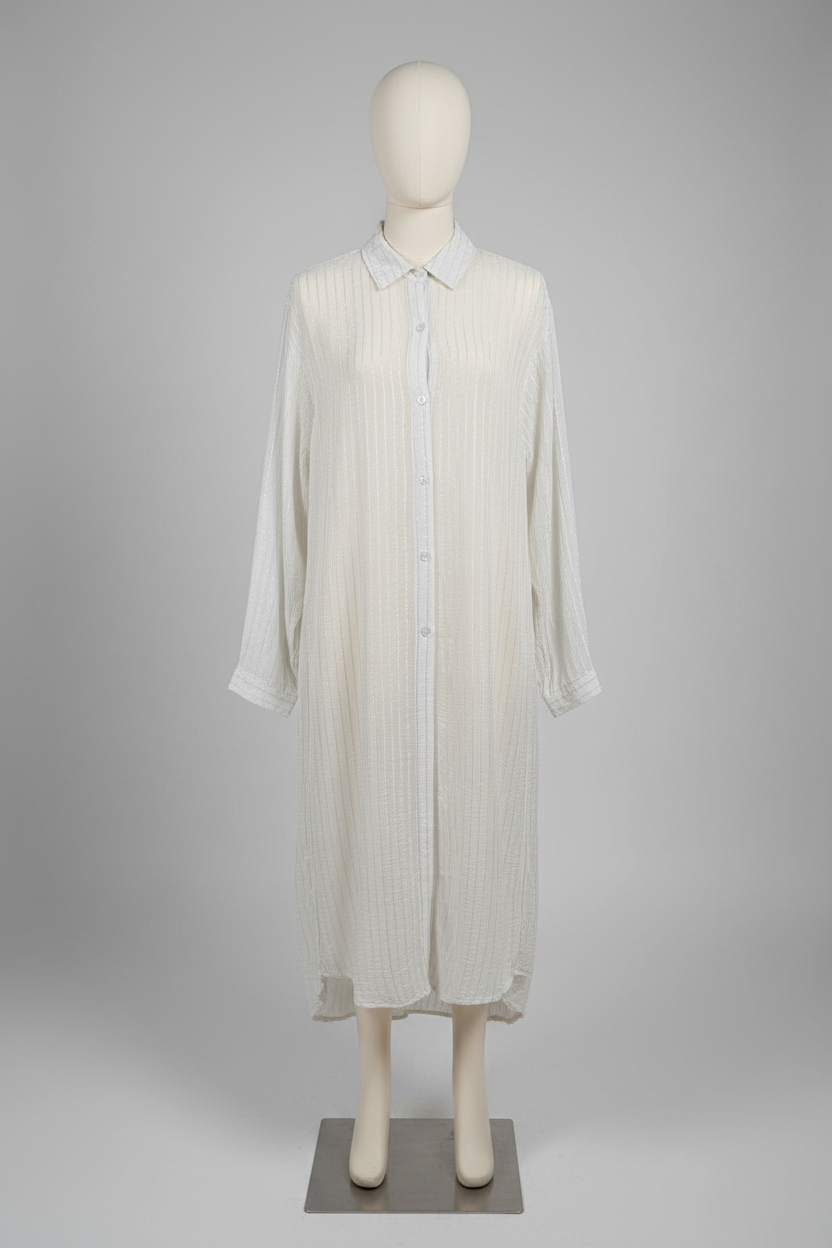 A woman models a long-sleeve, button-front shirt dress in a light gray and white vertical stripe pattern, styled with black wide-leg pants against a solid beige studio background.