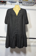A black short-sleeve button-front dress displayed on a yellow mannequin torso, hanging on a clothing rack against a white wall.