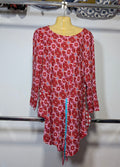 A red and white patterned long-sleeve tunic top with a tie-dye style floral design, hanging on a yellow mannequin torso on a clothing rack.