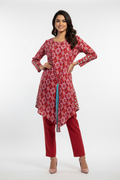 A woman modeling a red printed kurta with a blue and white tie detail, paired with matching red pants and nude heels, against a light gray studio background.
