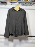 A black long-sleeve button-up shirt hanging on a yellow mannequin torso against a white wall, with clothing racks and other garments visible in the background.
