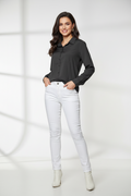 A woman modeling a black long-sleeve button-up shirt paired with white skinny jeans and white ankle boots, standing against a white studio background with soft window-like shadows.