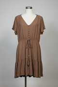 A brown short-sleeve V-neck dress displayed on a white mannequin torso against a light gray studio background. The dress has a gathered elastic waist with a drawstring and tassel, and a textured, slightly crinkled fabric.