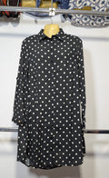 A black long-sleeve button-up shirt with white polka dots, displayed on a yellow hanger on a clothing rack.