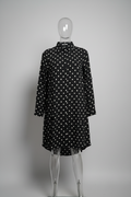 A black long-sleeve dress with a white polka-dot pattern, displayed on a clear acrylic mannequin against a neutral gray background.