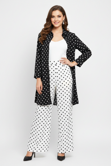 A woman models a black and white polka dot outfit consisting of a long-sleeve open-front cardigan, white top, white wide-leg pants, and black high heels against a light gray studio background.