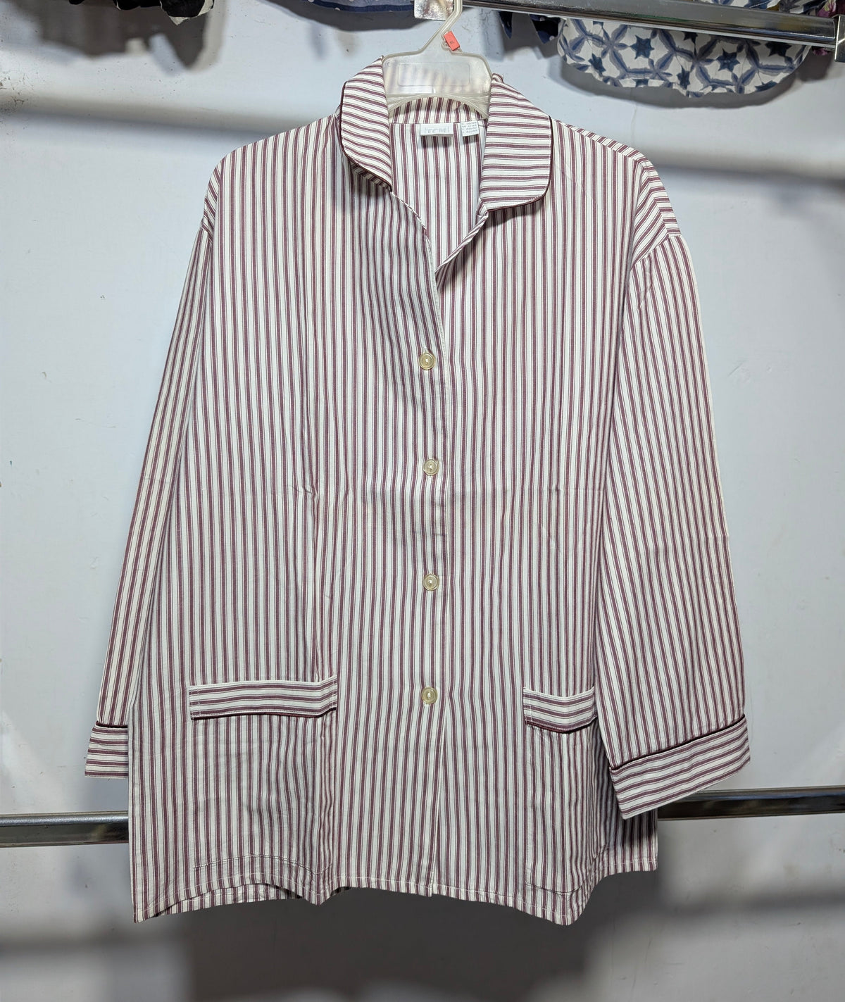 A long-sleeve button-front shirt with vertical brown and white stripes, hanging on a white plastic hanger against a light gray wall.