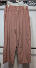 A pair of women's cropped pants in a dusty rose pink color with a small repeating red and white polka dot pattern, hanging on a white plastic hanger.