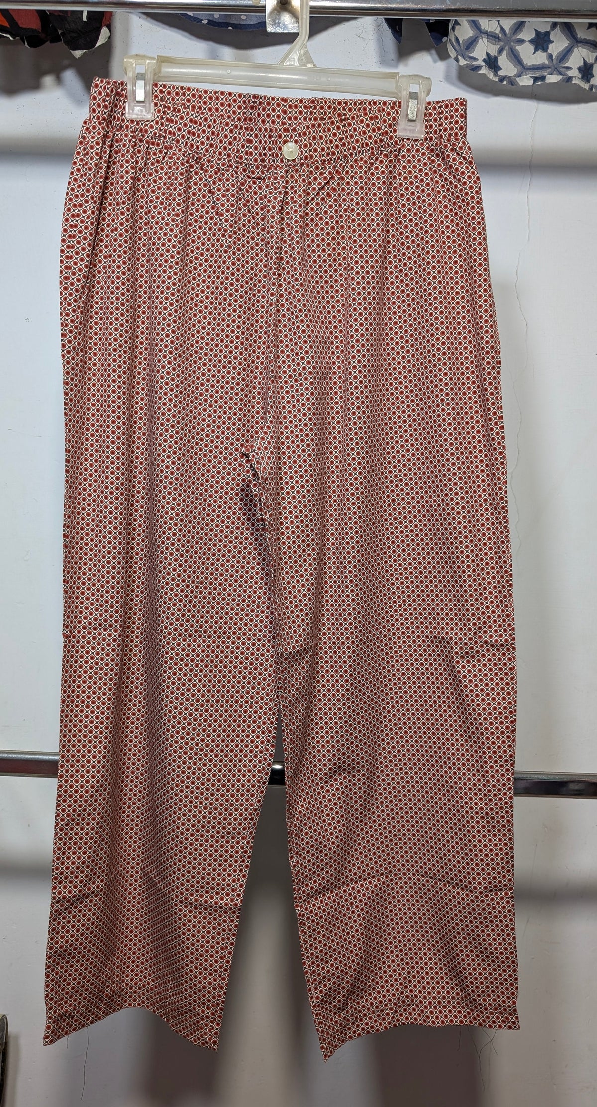 A pair of women's cropped pants in a dusty rose pink color with a small repeating red and white polka dot pattern, hanging on a white plastic hanger.
