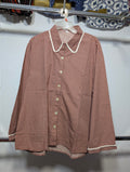 A long-sleeve button-up shirt with a small red and white polka dot pattern, featuring a white Peter Pan collar and white piping along the edges, hanging on a white hanger.