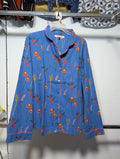 A blue long-sleeve button-up shirt with a colorful embroidered floral and botanical pattern, hanging on a white hanger against a white wall.