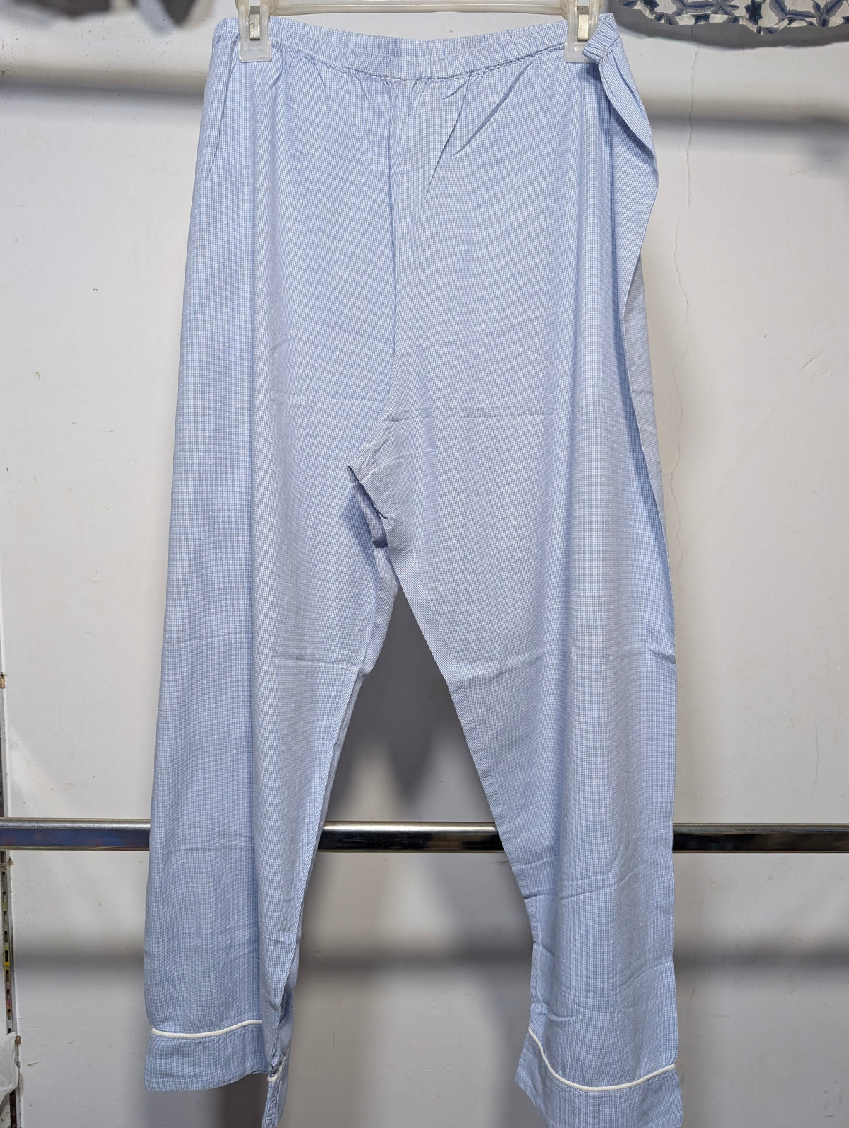 Light blue cropped pants with a relaxed, baggy fit and rolled cuffs, hanging on a white plastic hanger against a white wall.
