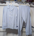 A light blue pajama set consisting of a long-sleeve button-front top with white piping and matching loose pants, hanging on hangers on a clothing rack.
