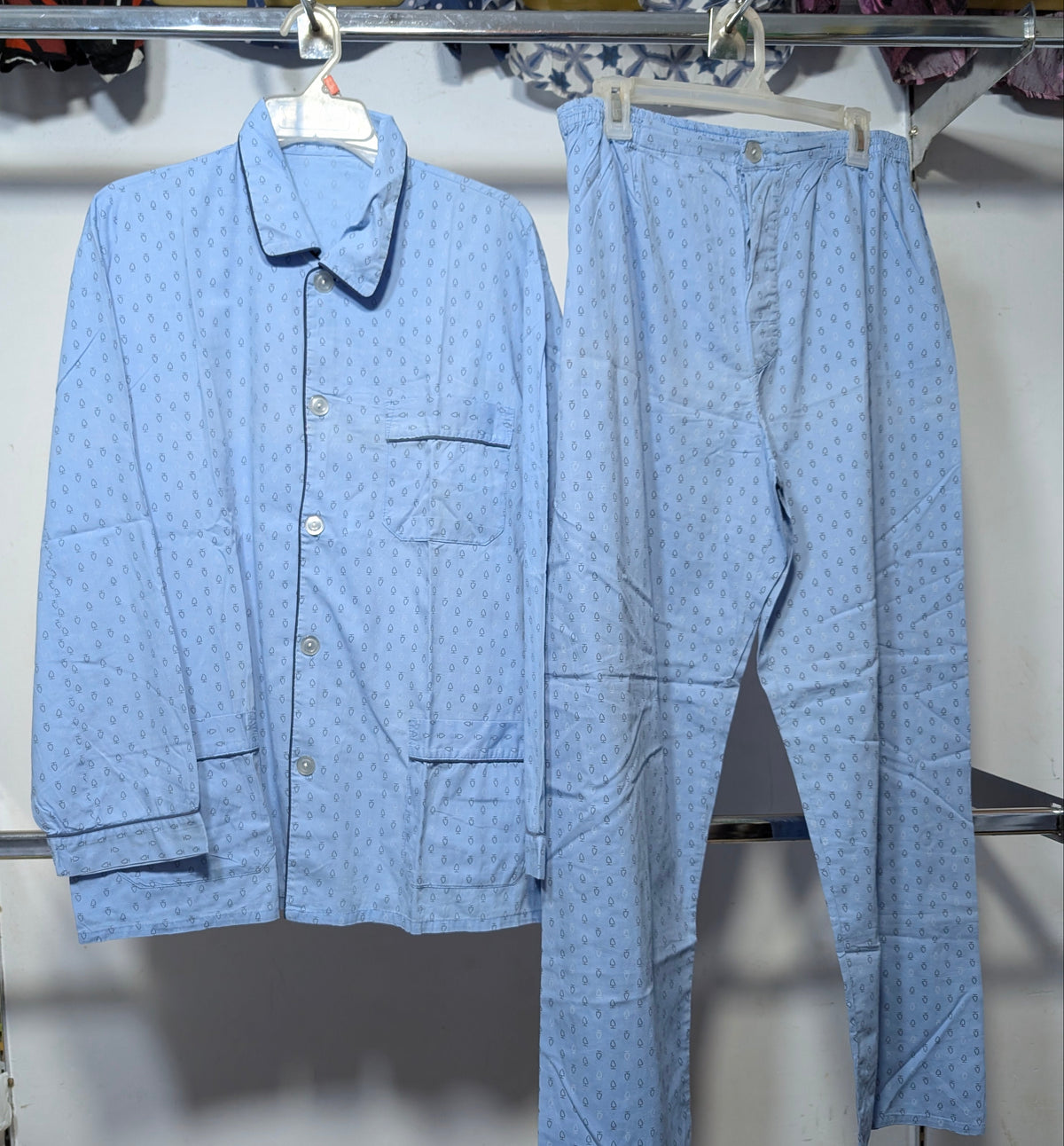 A light blue two-piece pajama set with a small repeating pattern, consisting of a long-sleeve button-front shirt and matching pants, hanging on a clothing rack.