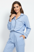A woman modeling a light blue patterned pajama set with black piping details, consisting of a long-sleeve button-up shirt and matching pants, against a plain light gray background.