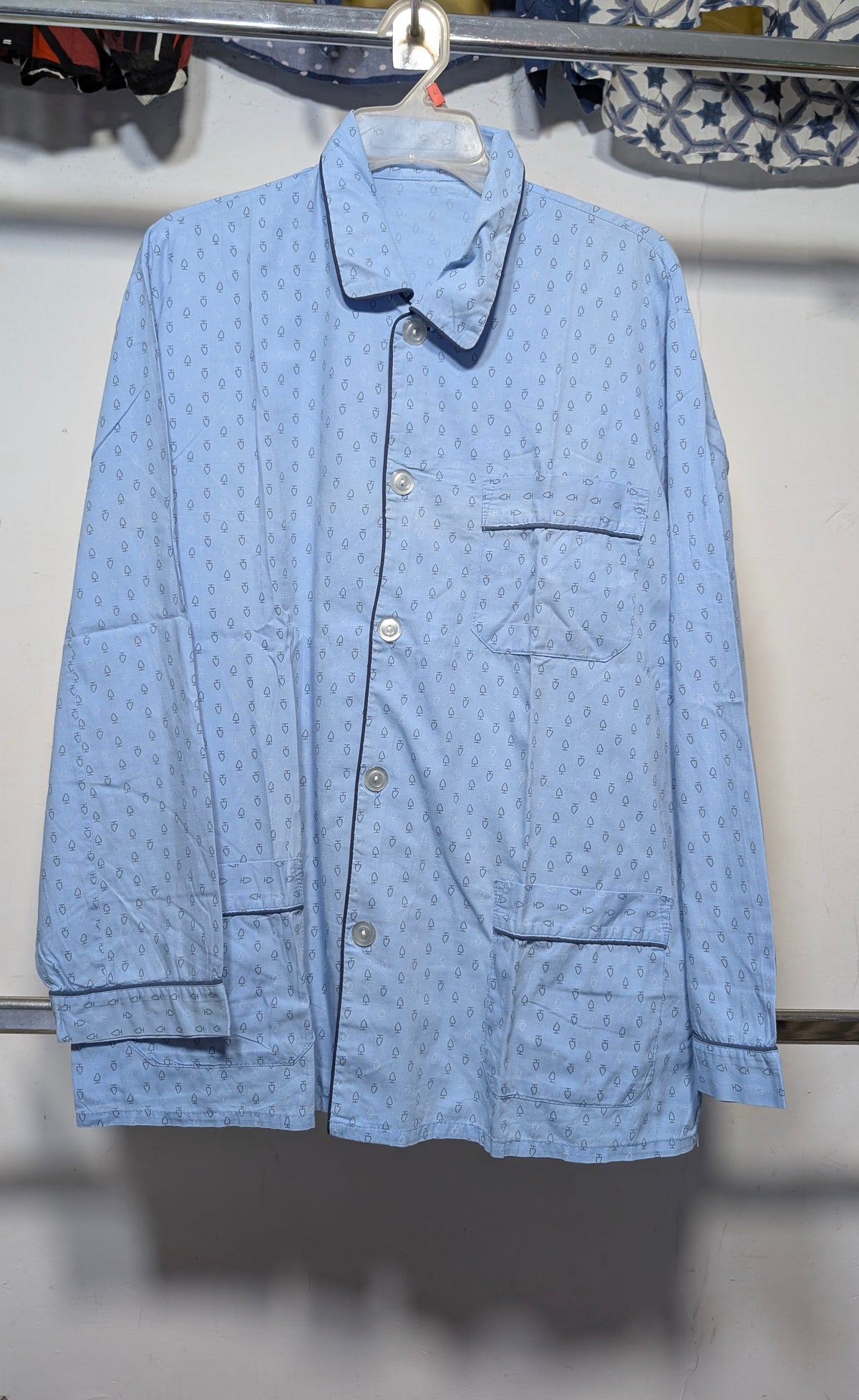 A light blue long-sleeve button-up shirt with a subtle repeating pattern, hanging on a white hanger against a white wall.