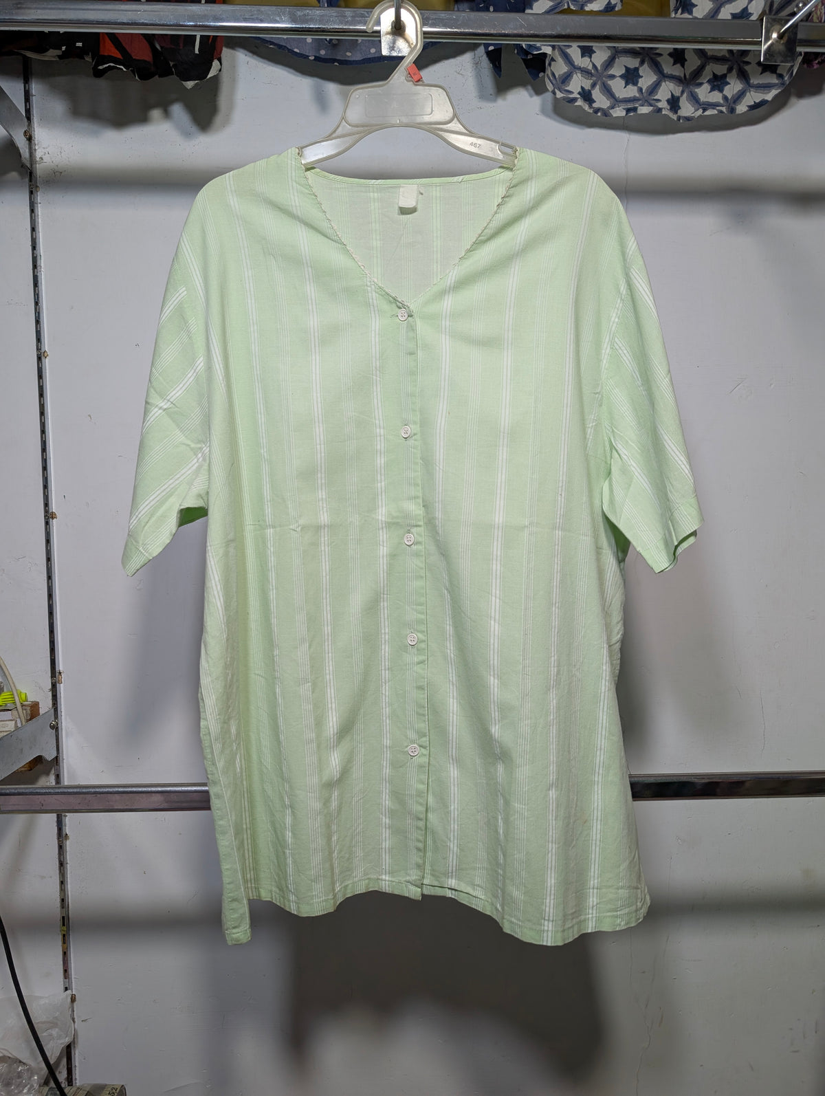 A light green short-sleeve button-up shirt with vertical white stripes, hanging on a white plastic hanger on a clothing rack.