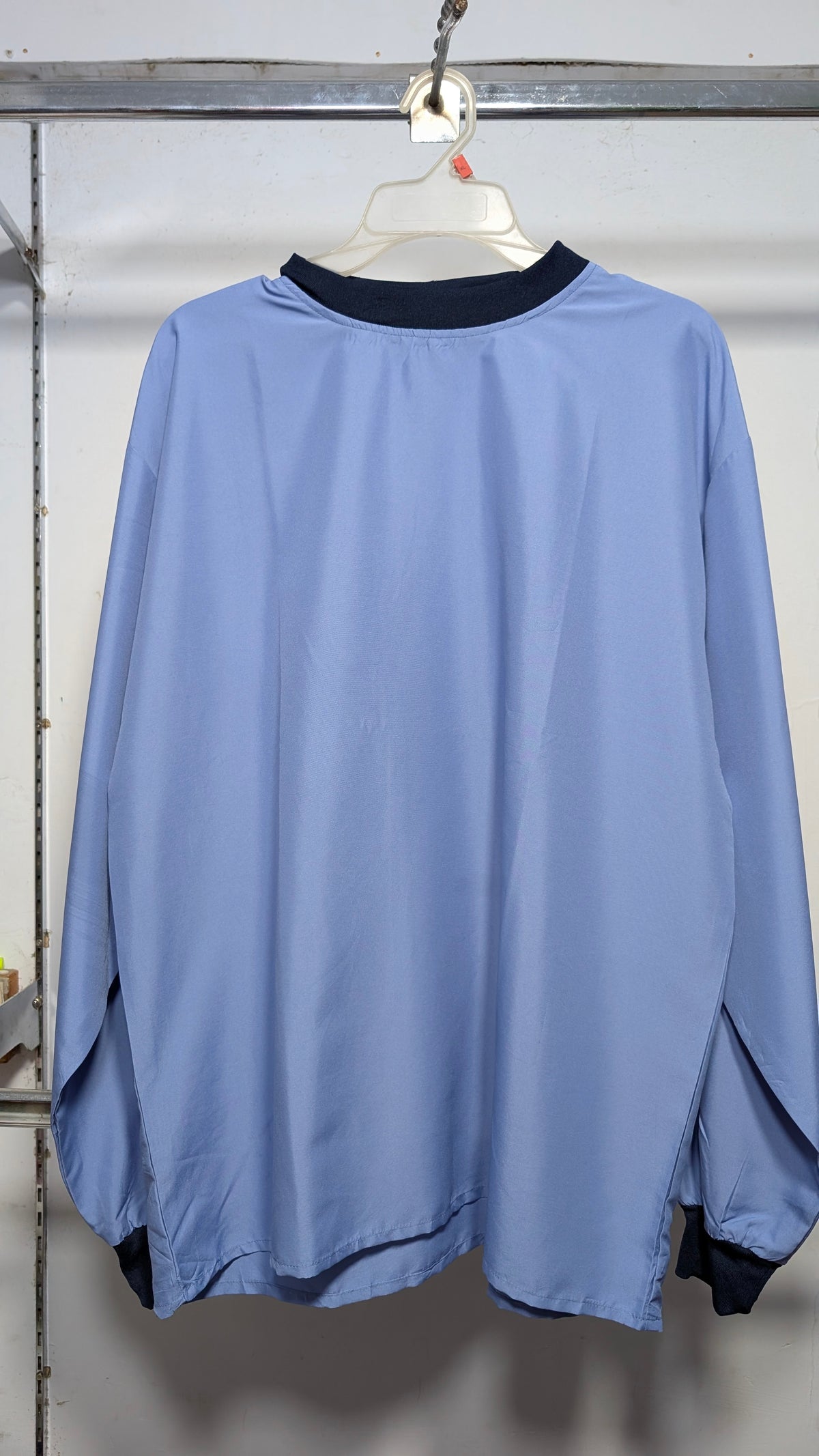 A light blue long-sleeve windbreaker jacket with a dark navy collar, hanging on a white plastic hanger from a metal clothing rack.