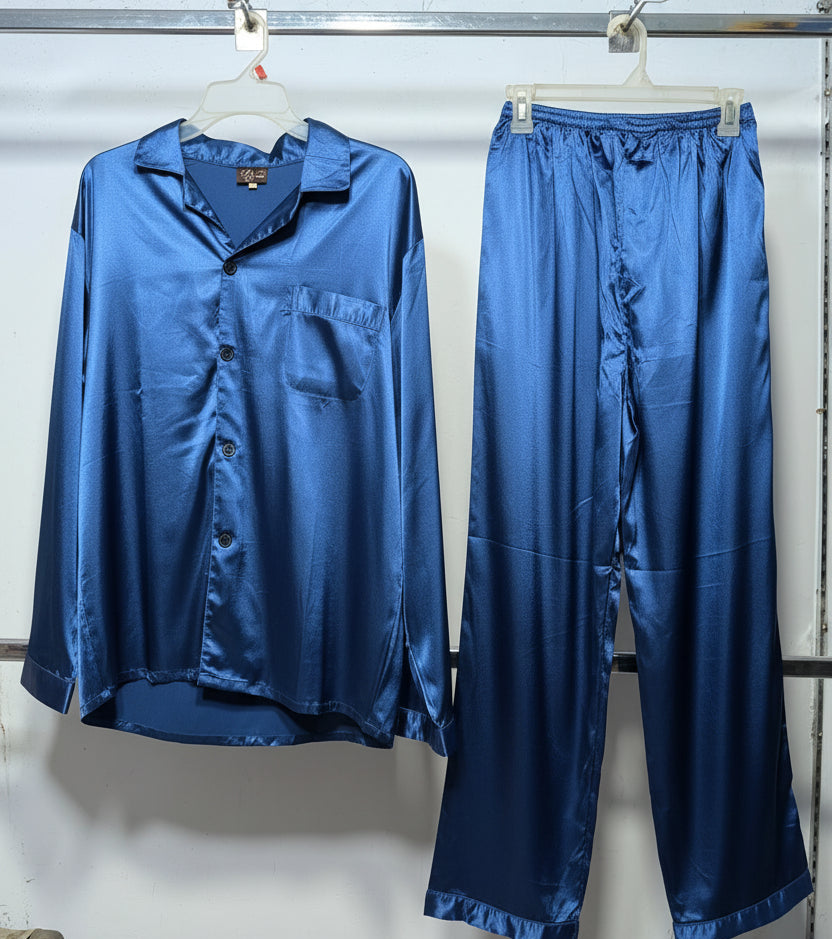 A two-piece satin pajama set in a rich blue color, consisting of a long-sleeve button-up shirt and matching pants, hanging on hangers against a white wall.