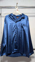 A long-sleeve satin button-up shirt in a deep blue color, hanging on a white plastic hanger against a white wall.
