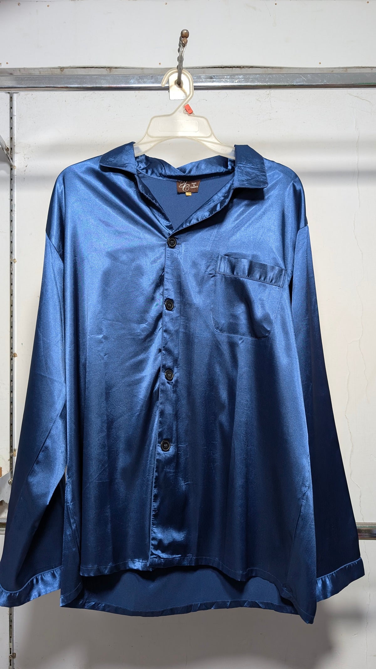 A long-sleeve satin button-up shirt in a deep blue color, hanging on a white plastic hanger against a white wall.