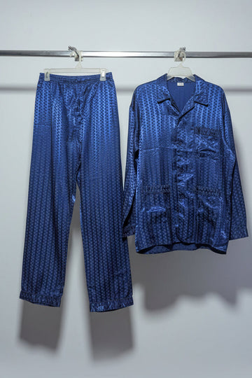 Blue patterned shirt and pants hanging on a rack against a white wall.