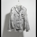 Silver floral blouse on a hanger against a white wall
