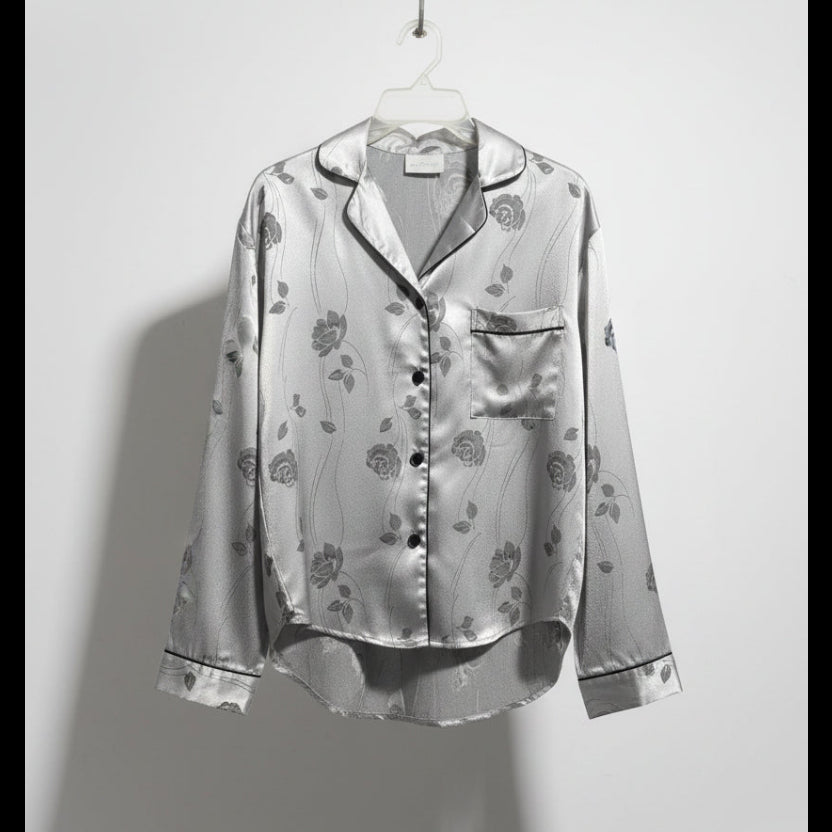 Silver floral blouse on a hanger against a white wall