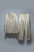 Gold satin suit jacket and pants hanging on a rack against a white wall.
