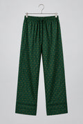 Green patterned pants hanging on a metal hanger against a white wardrobe door.