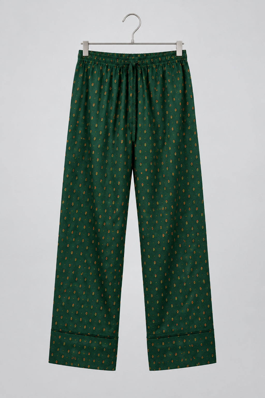Green patterned pants hanging on a metal hanger against a white wardrobe door.