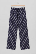 A pair of dark purple cropped pants with a light pink paisley pattern, hanging on a metal hanger against a white wardrobe door.