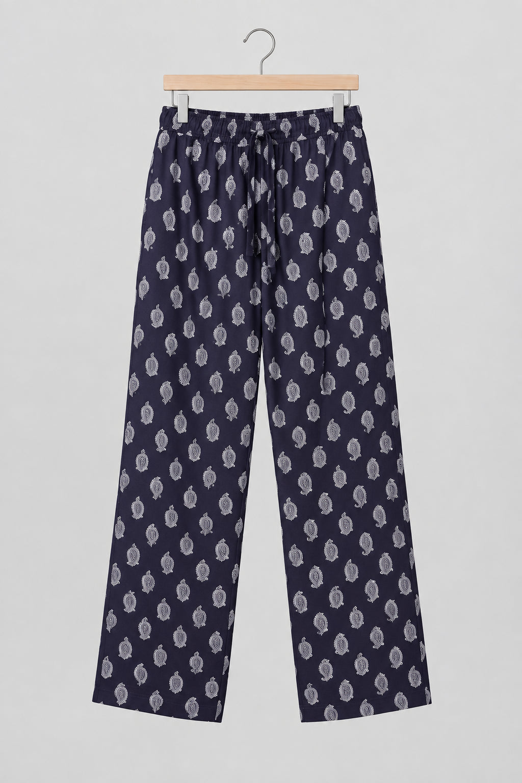 A pair of dark purple cropped pants with a light pink paisley pattern, hanging on a metal hanger against a white wardrobe door.