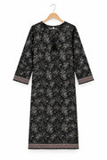 A black three-quarter sleeve tunic dress with a white floral print and patterned trim, hanging on a metal hanger against a white wardrobe door.