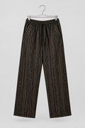 A pair of loose-fitting cropped pants with vertical black, brown, and orange stripes, hanging on a metal hanger against a white wardrobe door.