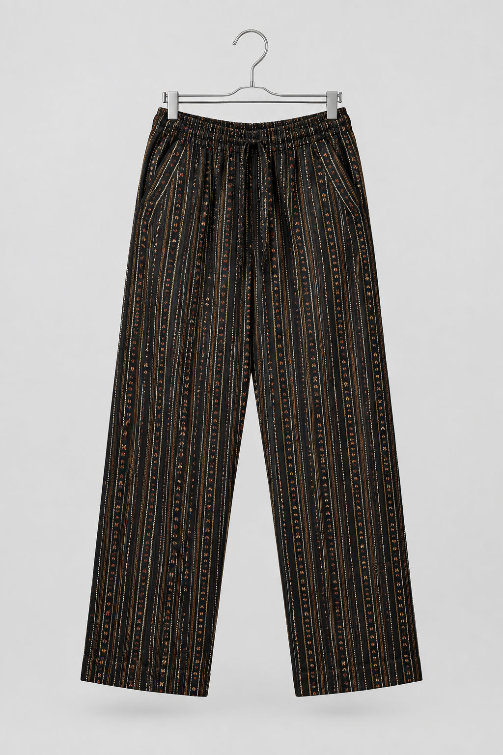 A pair of loose-fitting cropped pants with vertical black, brown, and orange stripes, hanging on a metal hanger against a white wardrobe door.