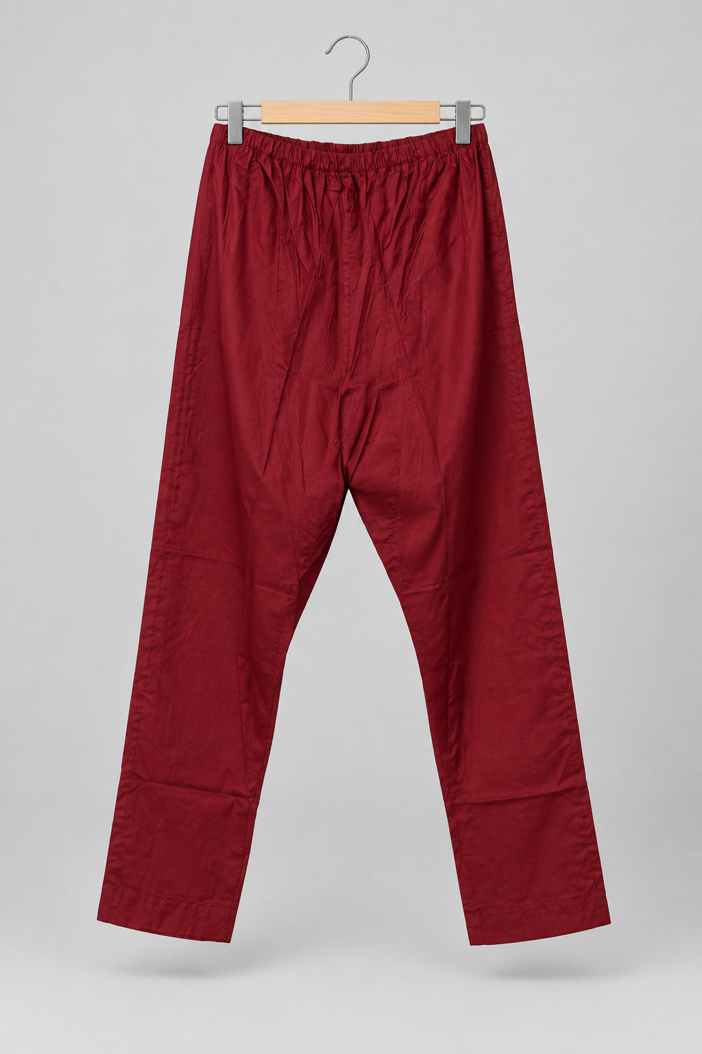 A pair of loose-fitting, cropped red pants with an elastic waistband and wide legs, hanging on a metal hanger against a white wardrobe door.