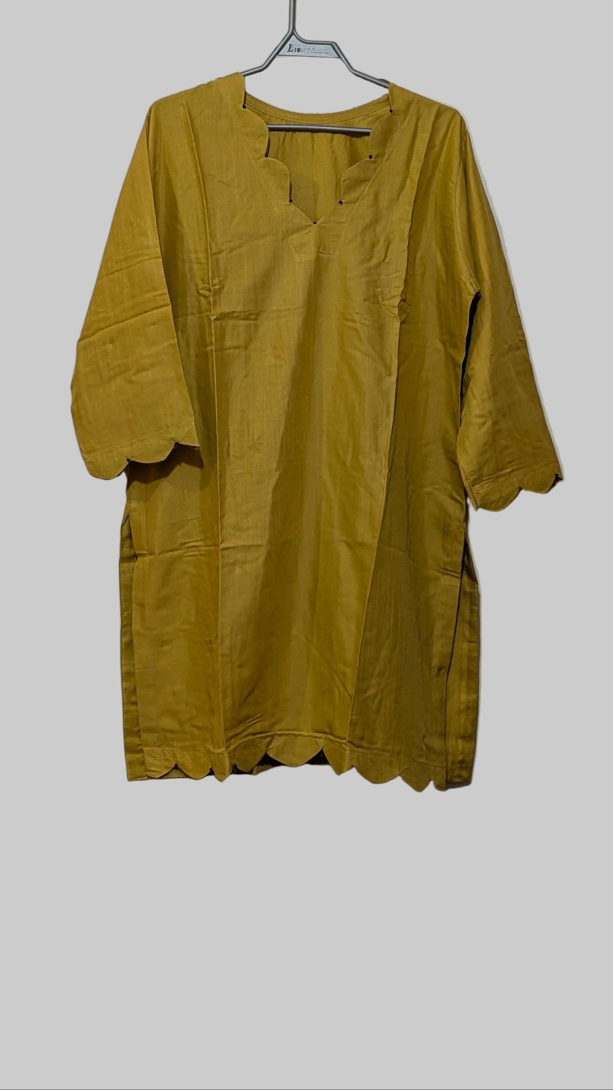 A mustard yellow tunic top with scalloped edges and elbow-length sleeves, hanging on a metal hanger against a white wardrobe door.