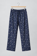 A pair of dark navy blue pants with a white snowflake pattern, hanging on a metal hanger against a white wardrobe door.