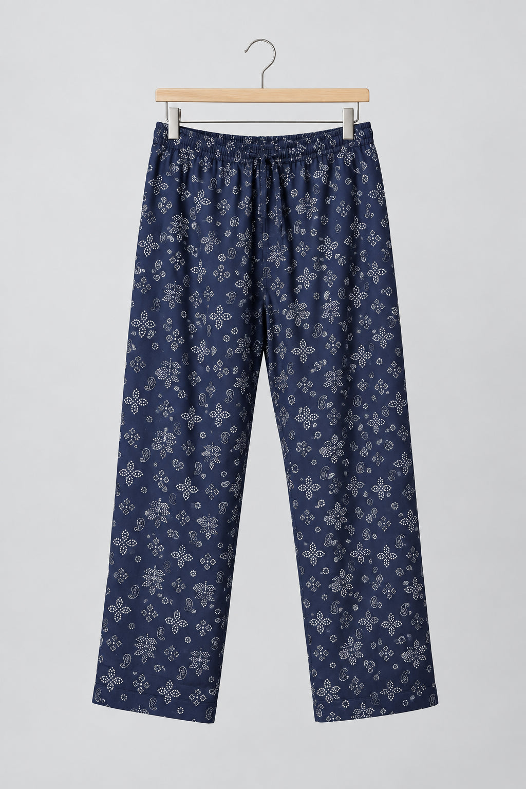 A pair of dark navy blue pants with a white snowflake pattern, hanging on a metal hanger against a white wardrobe door.