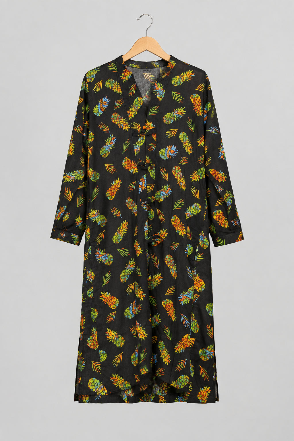A black long-sleeve tunic or robe with a colorful all-over leaf print, hanging on a metal hanger against a white wardrobe door.
